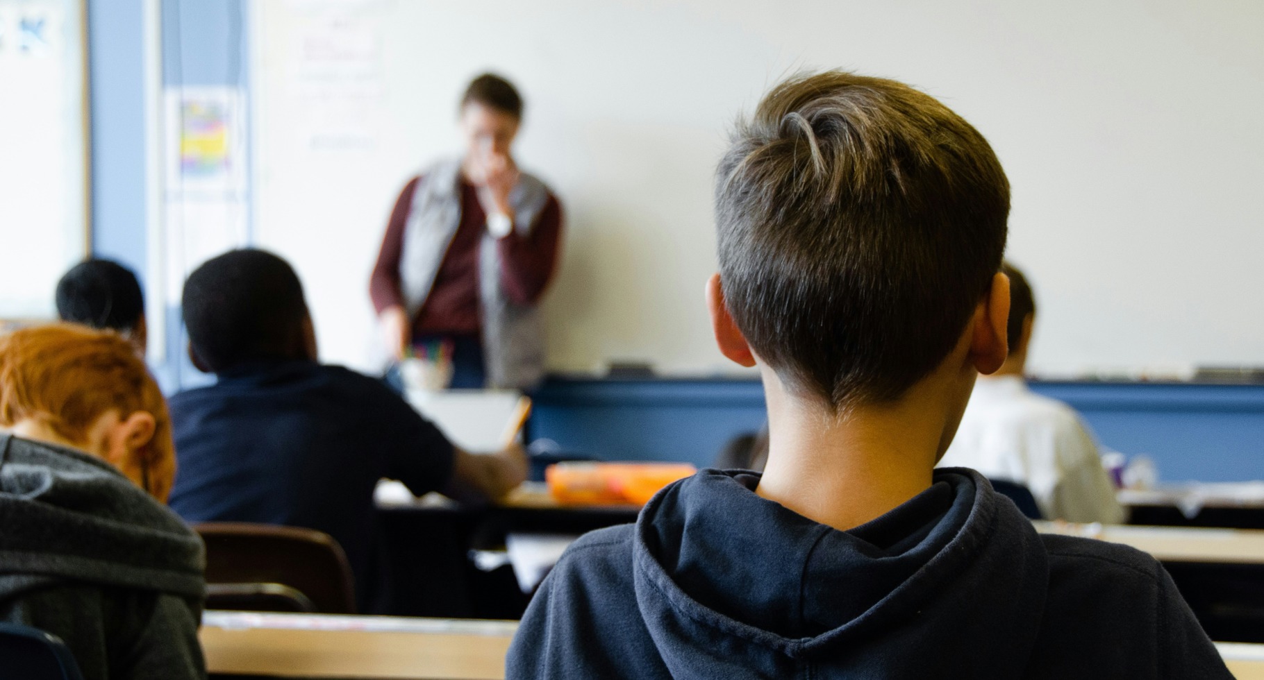 Elev set bagfra i klasseværelse mens lærer underviser ved tavlen.