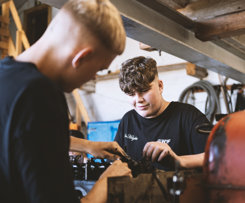 To elever reparerer gammel traktormotor i værksted.